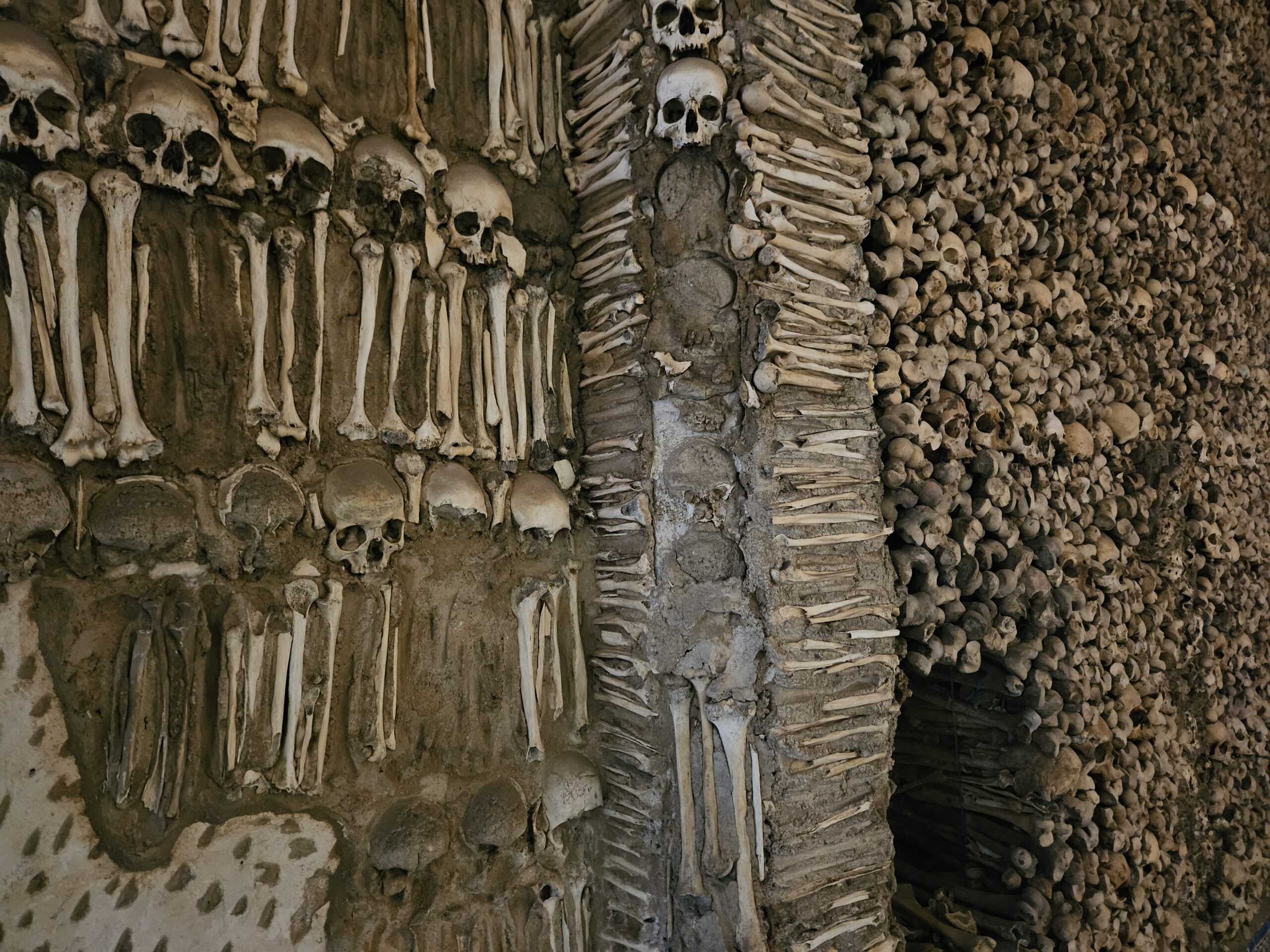 Paredes e pilares são revestidos com ossos e crânios humanos, cuidadosamente dispostos, ligados por cimento pardo