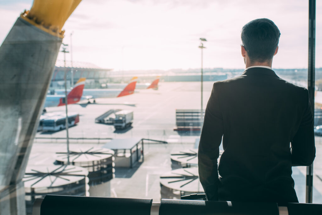 atras de um jovem empresario de pe com mala no aeroporto esperando o voo xa Incomum Viagens aposta em premiação garantida para agentes no aniversário de 27 anos